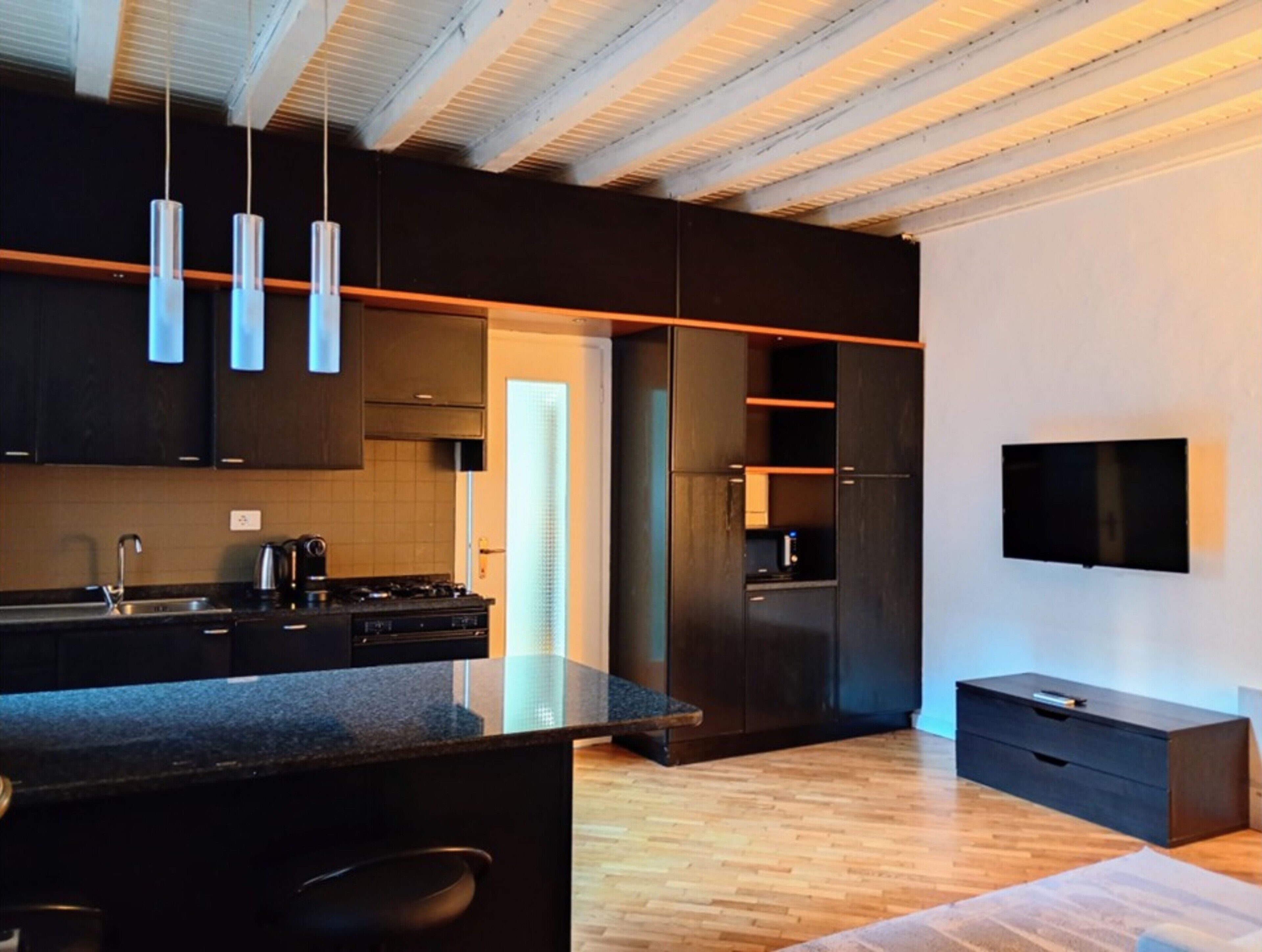 Une cuisine moderne avec des meubles de couleur sombre, un îlot central et des luminaires suspendus.