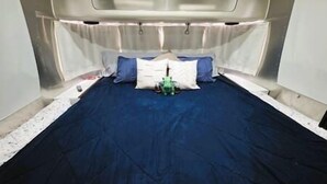 Een kleine, goed verlichte kamer met een eenpersoonsbed, kussens en een klein, groen voorwerp op het bed.