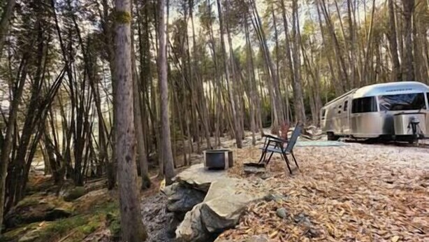 Een camping met een tent, een stoel en een camper, geparkeerd op een onverharde ondergrond, omringd door bomen.