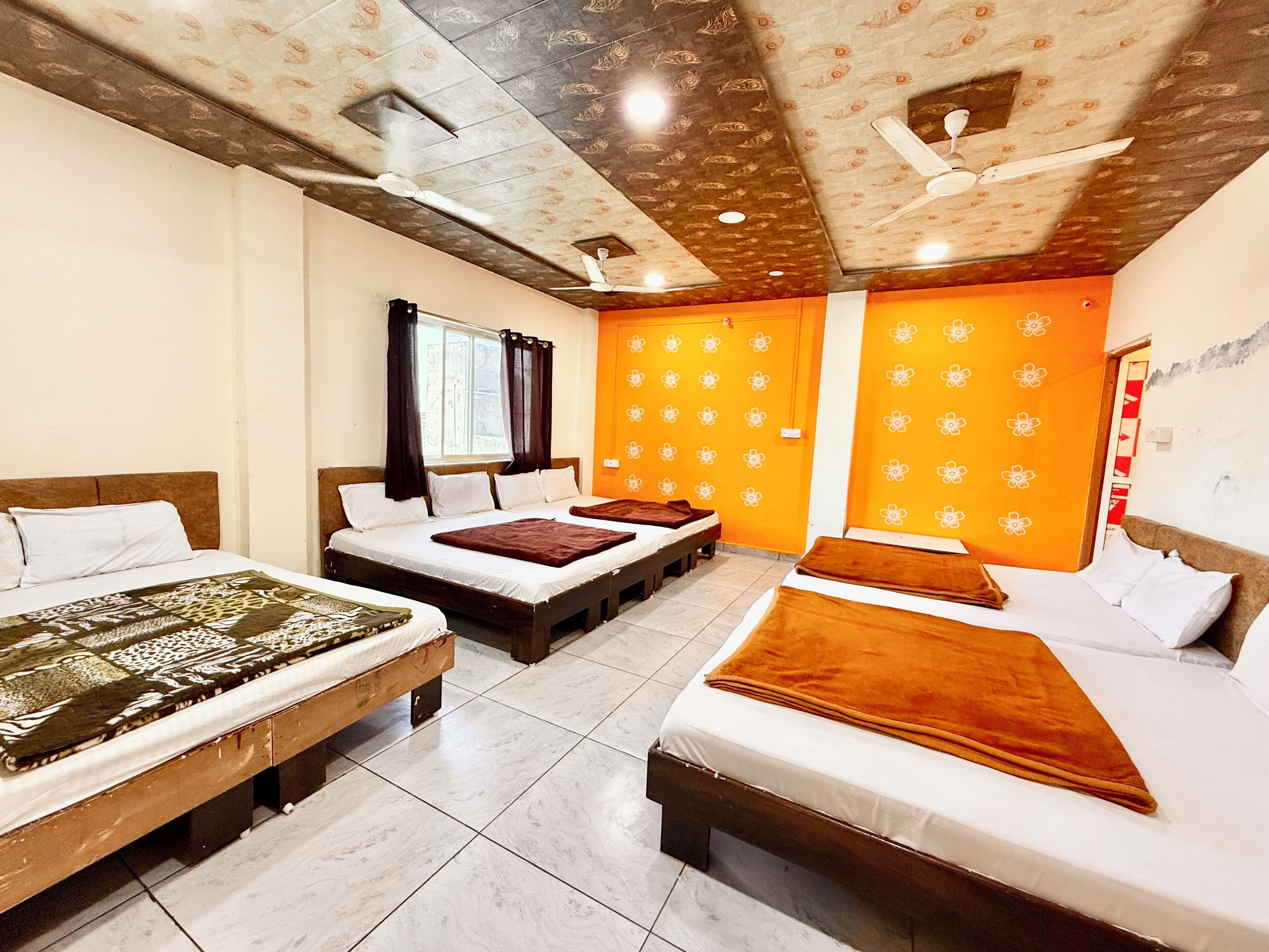 Een hotelkamer met drie bedden, een raam met gordijnen, een oranje muur met bloemendesign en een plafond met bloemdecoratie.