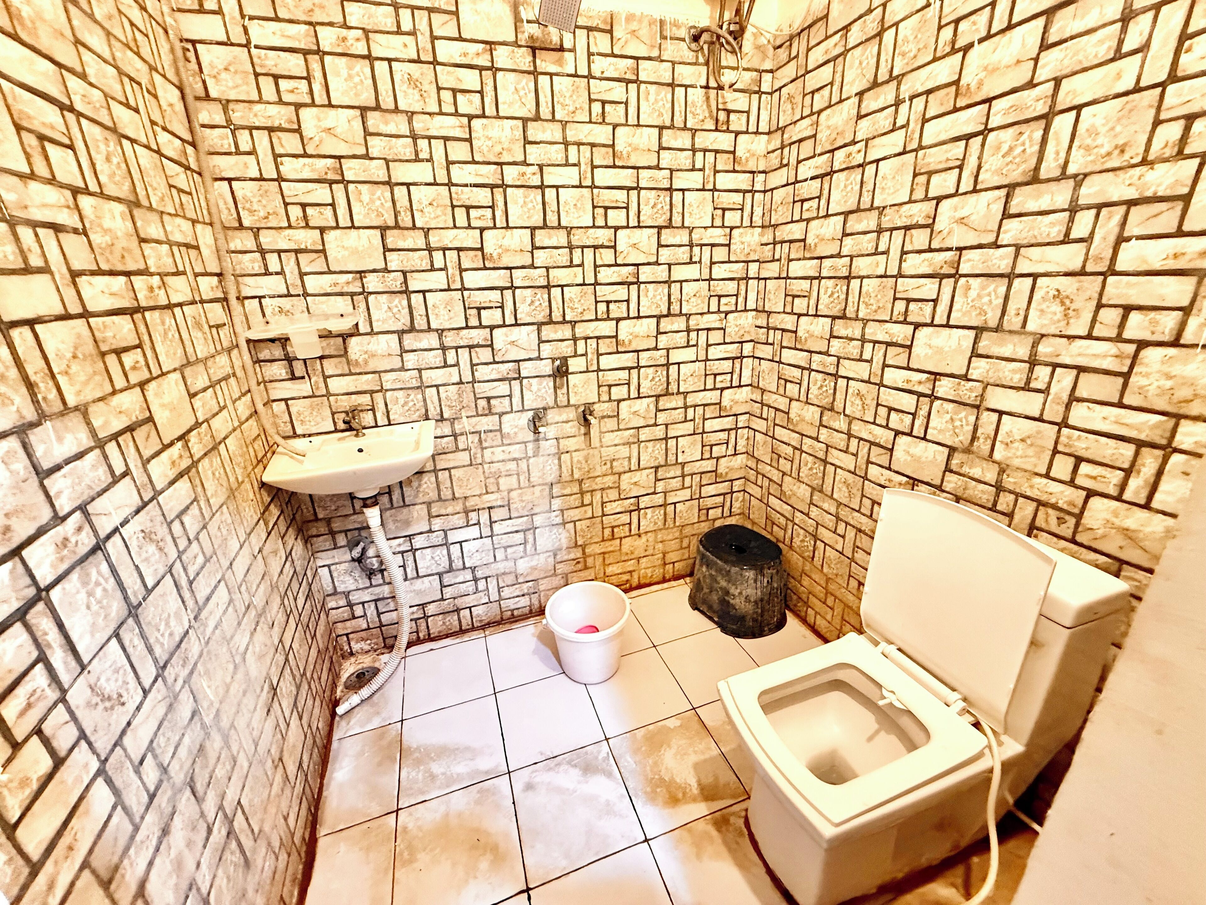 A small bathroom with a toilet, a sink, and a bucket.