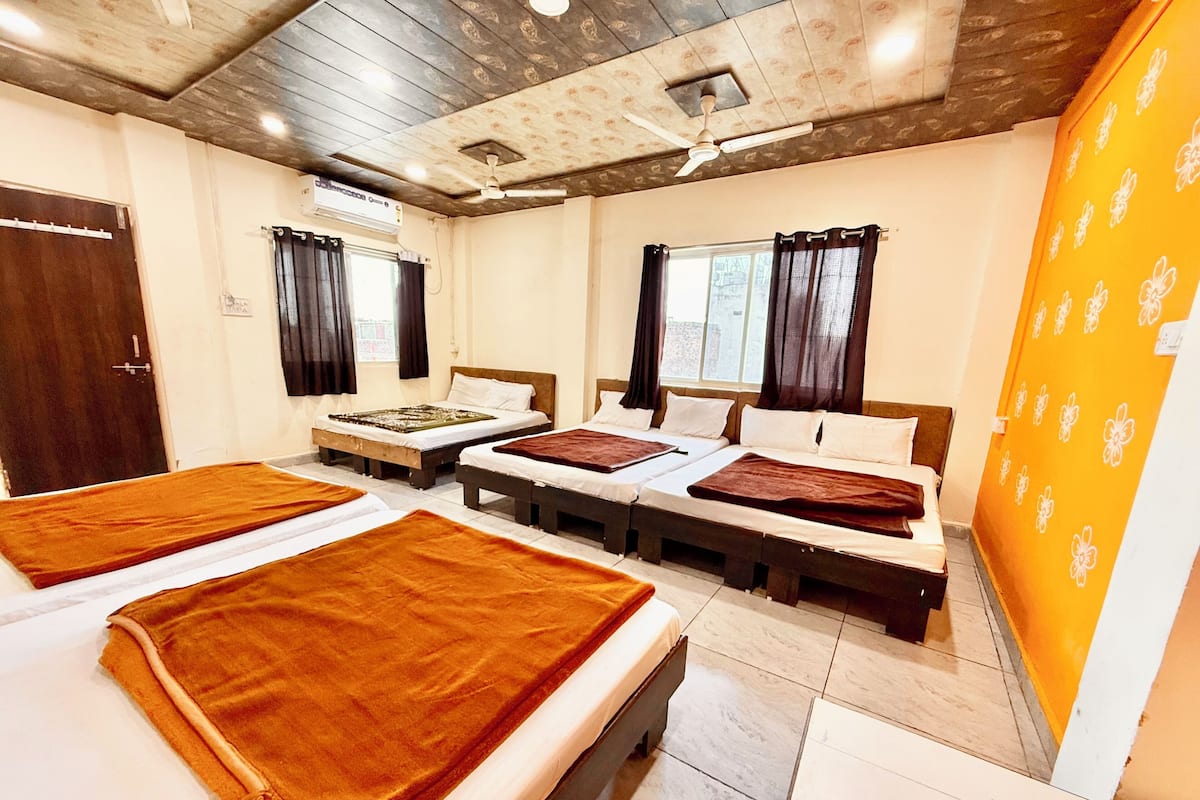 Une chambre d’hôtel avec quatre lits, un ventilateur de plafond, un appareil de climatisation et une fenêtre avec des rideaux.