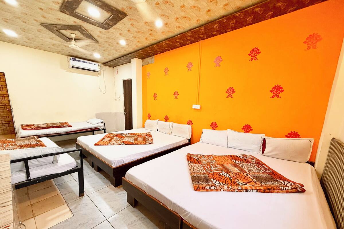 Une chambre d’hôtel avec trois lits, un appareil de climatisation et un mur orange à motifs.