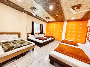 Une chambre d’hôtel avec deux lits, une fenêtre avec des rideaux, un mur orange orné d’un motif floral et un ventilateur de plafond.