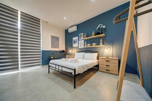 Ein Schlafzimmer mit einem Bett, Nachttischen, Ablageflächen und einem Fenster mit Jalousien.