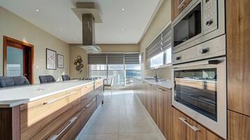 A modern kitchen with wooden cabinets, stainless steel appliances, a large island with seating, and a view to the outdoors.