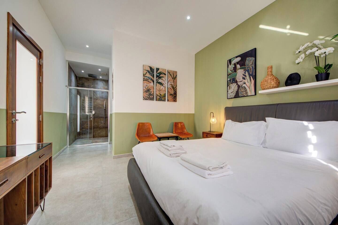 A hotel room with a large bed, two chairs, a desk, and a shower area.