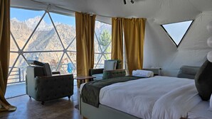 A bedroom with a large bed, a sofa, a small table, and a window overlooking mountains. - The Glamp Hills Auli (Joshimath)