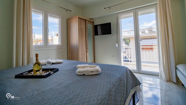 Una habitación de hotel con cama, televisor montado en la pared y balcón con cortinas.