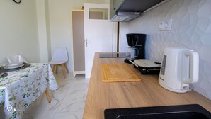 Una cocina con encimera de madera, un hervidor blanco y una zona de comedor con una mesa para dos.