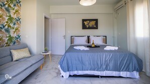 Un dormitorio con cama, sofá, una mesita con una botella y vasos, un mapa del mundo en la pared y una lámpara en el techo.