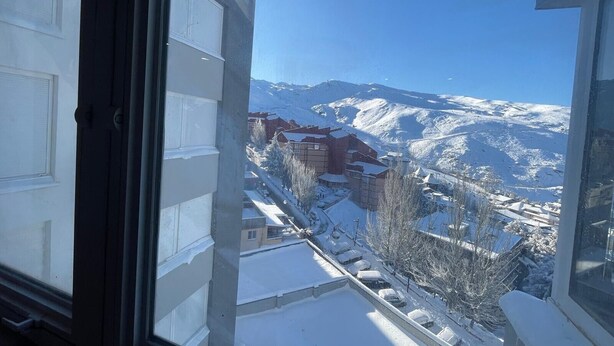 Aussicht auf verschneite Berge vom Fenster aus, mit Gebäuden und blauem Himmel.
