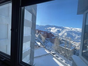 Vista nevada de una montaña desde una ventana, con edificios y un cielo despejado.