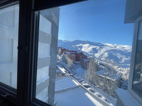 A snowy mountain view from a window, with buildings and a clear sky.