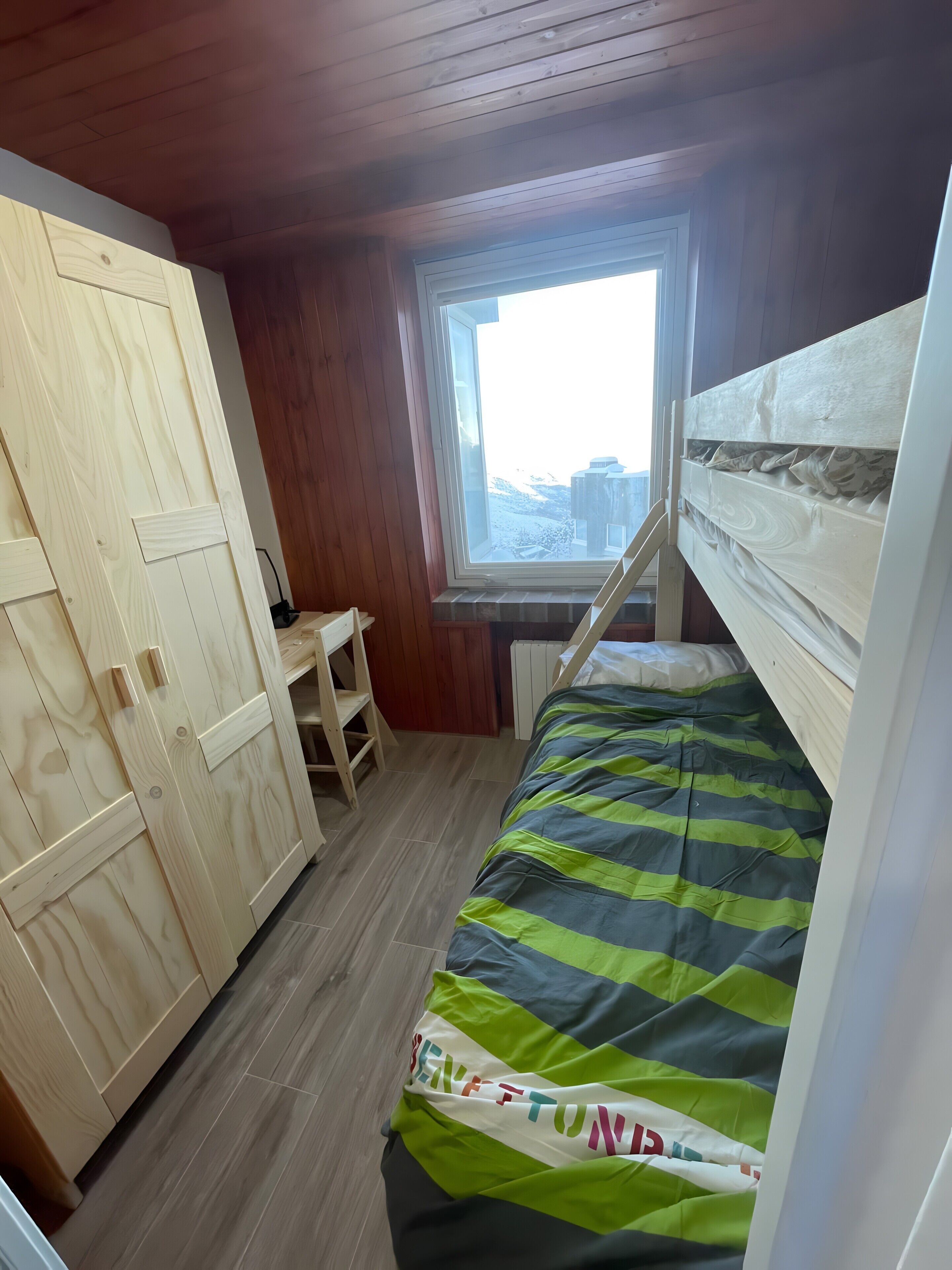 Une chambre avec un lit superposé, une armoire en bois et une fenêtre donnant sur un beau paysage.