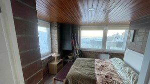 Ein Schlafzimmer mit einem Bett, einer Bank, einem Kamin, Skiern und einem Fenster mit Blick.