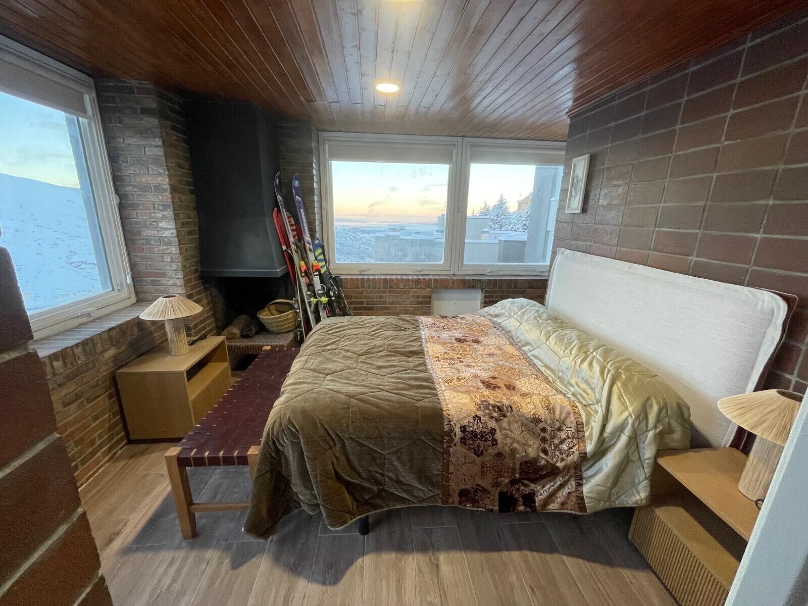 Ein Schlafzimmer mit Bett, einer Bank, einem Kamin, Skiern und Blick ins Freie.