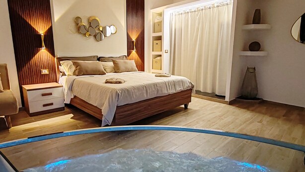 A bedroom with a bed, bedside tables, a nightstand, a wall-mounted mirror, and a window with curtains. - SIKELIA HOUSE - COMFORT APARTMENT Hospitality and elegance in the heart of Palermo (Palermo)