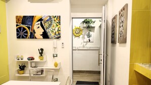 A modern interior with a dining area, a white table, and chairs. There are decorative items on shelves, a wall clock, and a door leading to another room. - SIKELIA HOUSE - COMFORT APARTMENT Hospitality and elegance in the heart of Palermo (Palermo)
