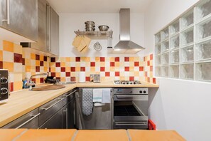 Une cuisine compacte dotée d’un plan de travail en bois, d’appareils électroménagers en acier inoxydable et d’un dosseret carrelé.