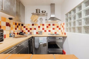 A compact kitchen with a wooden countertop, stainless steel appliances, and a tiled backsplash. - Brilliantly Located 1BDR Flat in West Kensington (Greater London)
