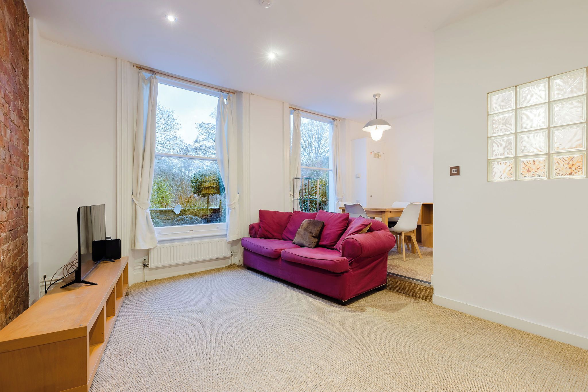 A modern living room with a red sofa, a television on a wooden stand, and large windows with curtains.