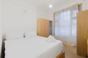 A bedroom with a bed, a wardrobe, and a window with curtains. - Brilliantly Located 1BDR Flat in West Kensington (Greater London)