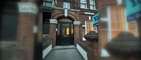 Un edificio de ladrillo con una puerta negra, un cartel que indica Palliser Road y un cartel de 'En venta'.