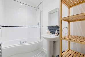 A modern bathroom with a freestanding bathtub, a sink, and a wooden shelf unit. - Brilliantly Located 1BDR Flat in West Kensington (Greater London)