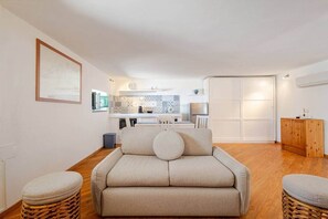 Ein kompakter Wohnraum mit Sofa, zwei Beistelltischen, Küchenzeile und Schiebetürenschrank.