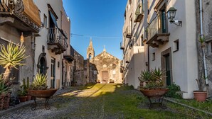 A cobblestone street with buildings on either side, a church with a bell tower, and potted plants. - Pietra Menalda - Apartment with sea-view terrace (Lipari)