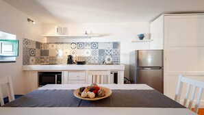 A compact kitchen with a tiled backsplash, a refrigerator, and a dining area with a table set for two. - Pietra Menalda - Apartment with sea-view terrace (Lipari)