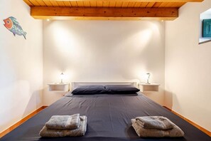 A bedroom with a bed, two bedside tables, two lamps, a wooden ceiling, and a fish decoration on the wall.