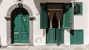 A building with a green door, green shutters, and a stone archway. - Pietra Menalda - Apartment with sea-view terrace (Lipari)