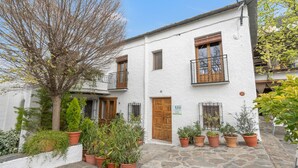 A white building with a stone-paved courtyard, wooden doors, and multiple potted plants. - Casa Pepa in Pampaneira – Charming Holiday Home in the Heart of La Alpujarra (Pampaneira)