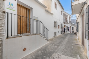 Un carrer estret amb edificis blancs, una porta de fusta i una barana de metall.