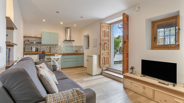 A modern living room with a sofa, TV, and a kitchen in the background. - Casa Pepa in Pampaneira – Charming Holiday Home in the Heart of La Alpujarra (Pampaneira)