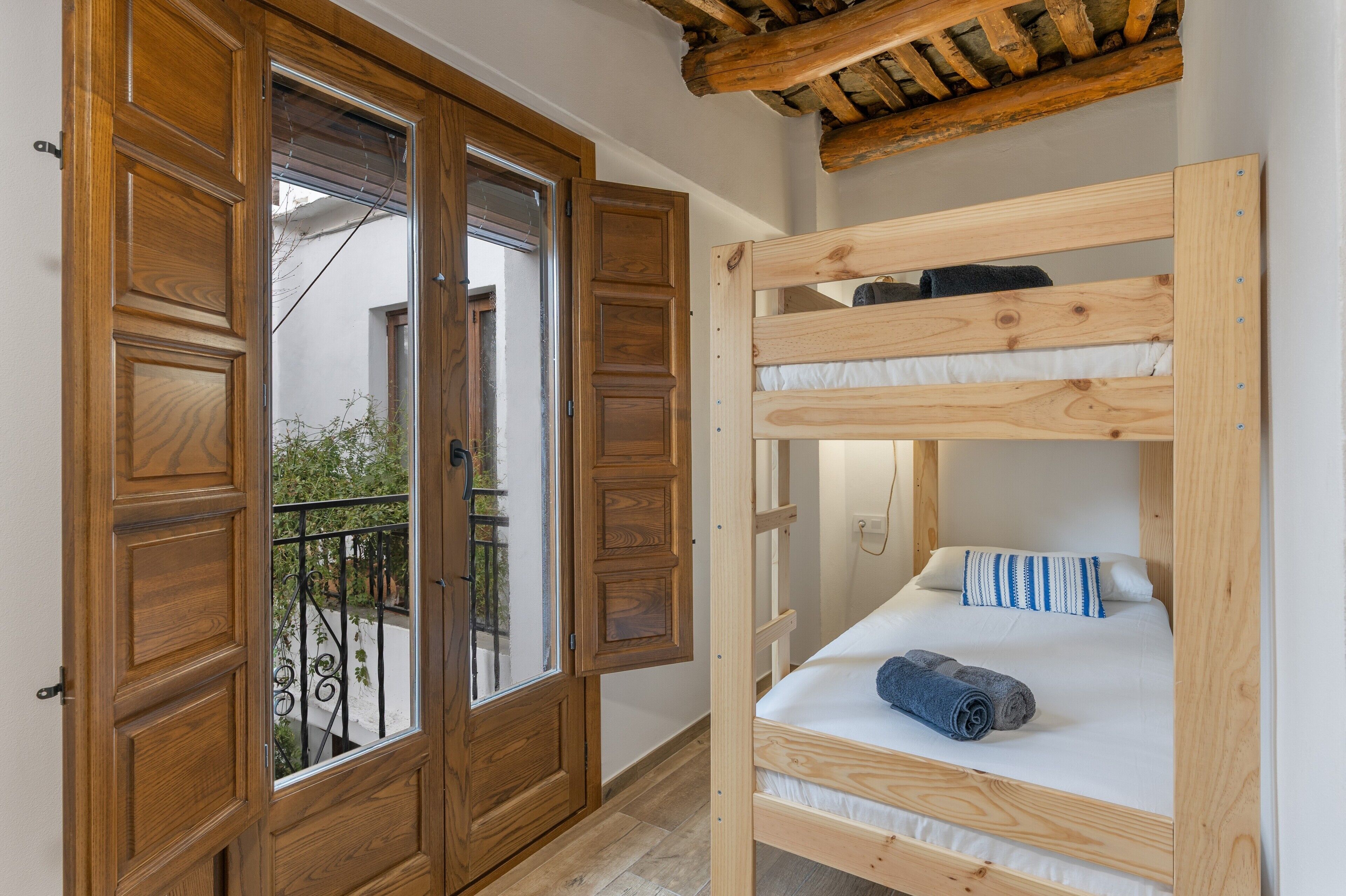 A room with a wooden bunk bed, a wooden door, and a balcony with a metal railing.