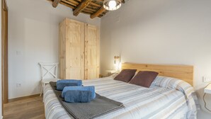 A bedroom with a wooden ceiling, a bed with striped bedding, a nightstand, and a wardrobe. - Casa Pepa in Pampaneira – Charming Holiday Home in the Heart of La Alpujarra (Pampaneira)
