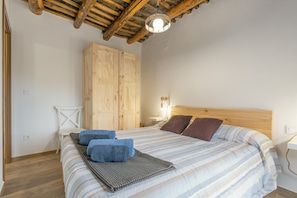 Un dormitorio con techo de madera, una cama con ropa de cama a rayas, una mesita de noche y un armario.