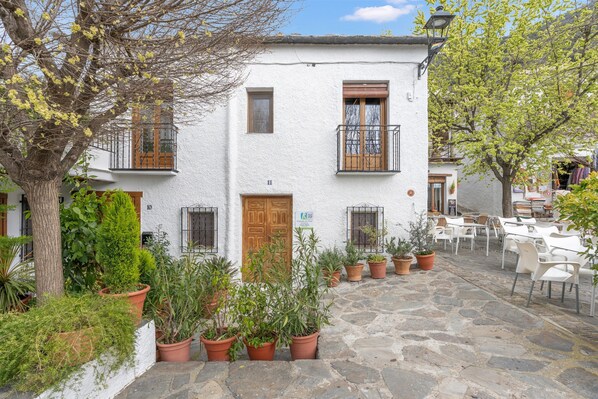 Une cour avec un bâtiment blanc, des plantes en pot et des sièges d’extérieur.