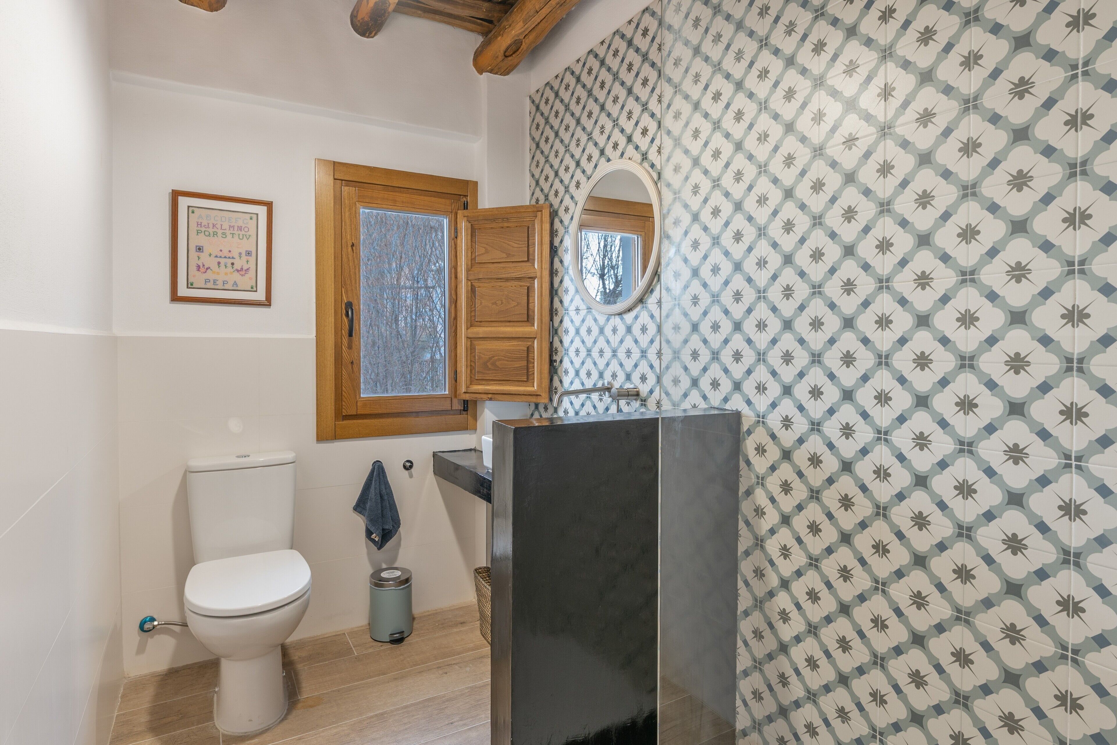 A bathroom with a toilet, a wooden cabinet, a mirror, and patterned wall tiles.