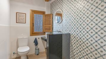 A bathroom with a toilet, a wooden cabinet, a mirror, and patterned wall tiles.