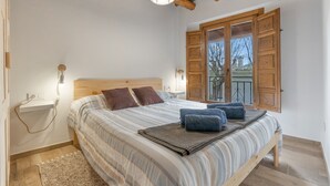 A bedroom with a wooden bed, a nightstand, a wall-mounted lamp, and a window with wooden shutters. - Casa Pepa in Pampaneira – Charming Holiday Home in the Heart of La Alpujarra (Pampaneira)