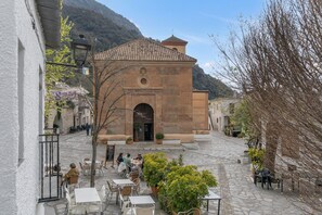 Une cour pavée avec des places assises à l’extérieur, un bâtiment avec un toit en tuiles et un paysage montagneux en arrière-plan.