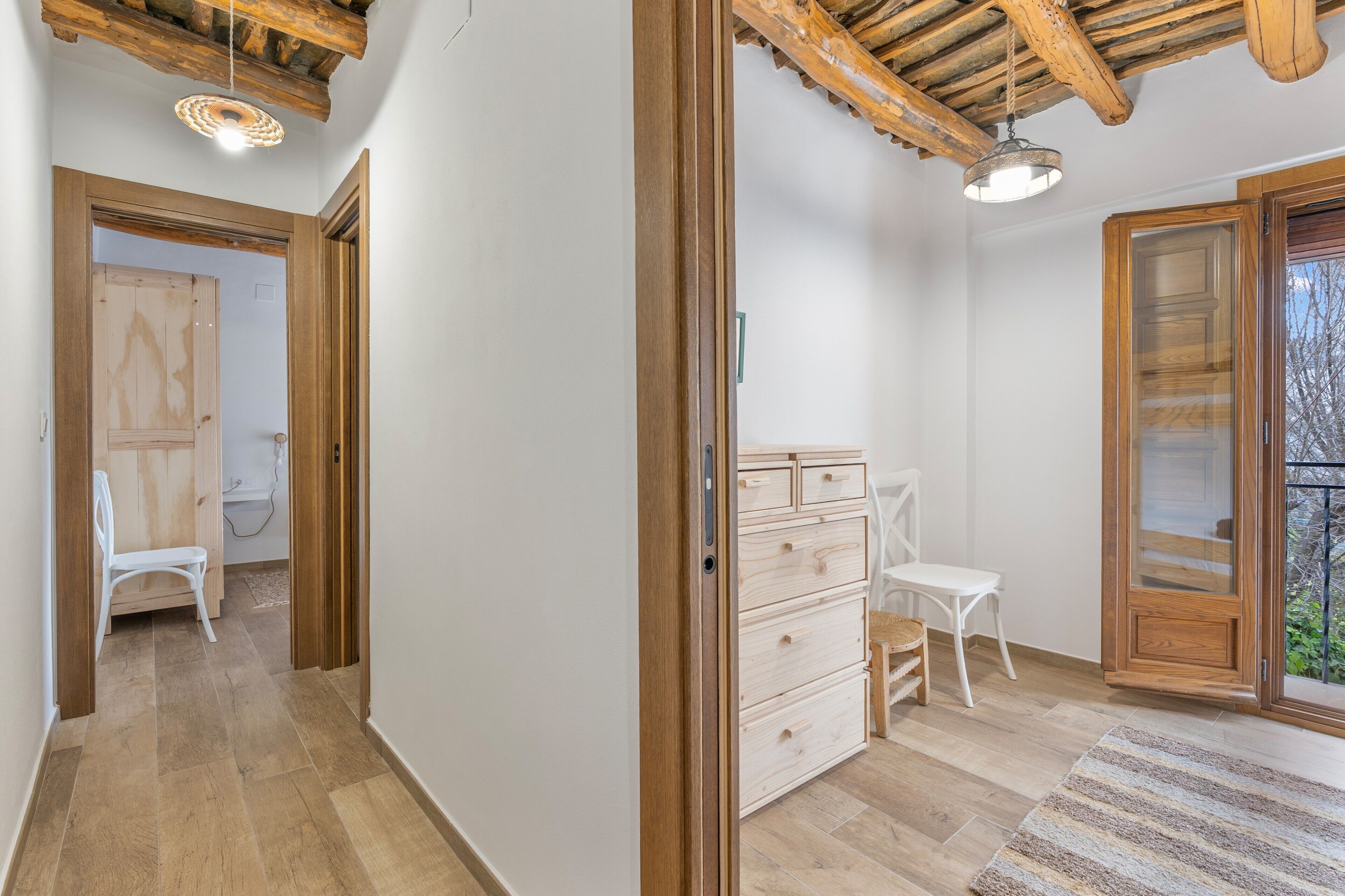 Une pièce avec un plafond en bois, un mur blanc, une porte en bois, une chaise blanche, une commode en bois et un tapis à rayures.