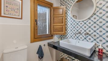 A bathroom with a white toilet, a sink with a mirror, a window, and patterned wallpaper.