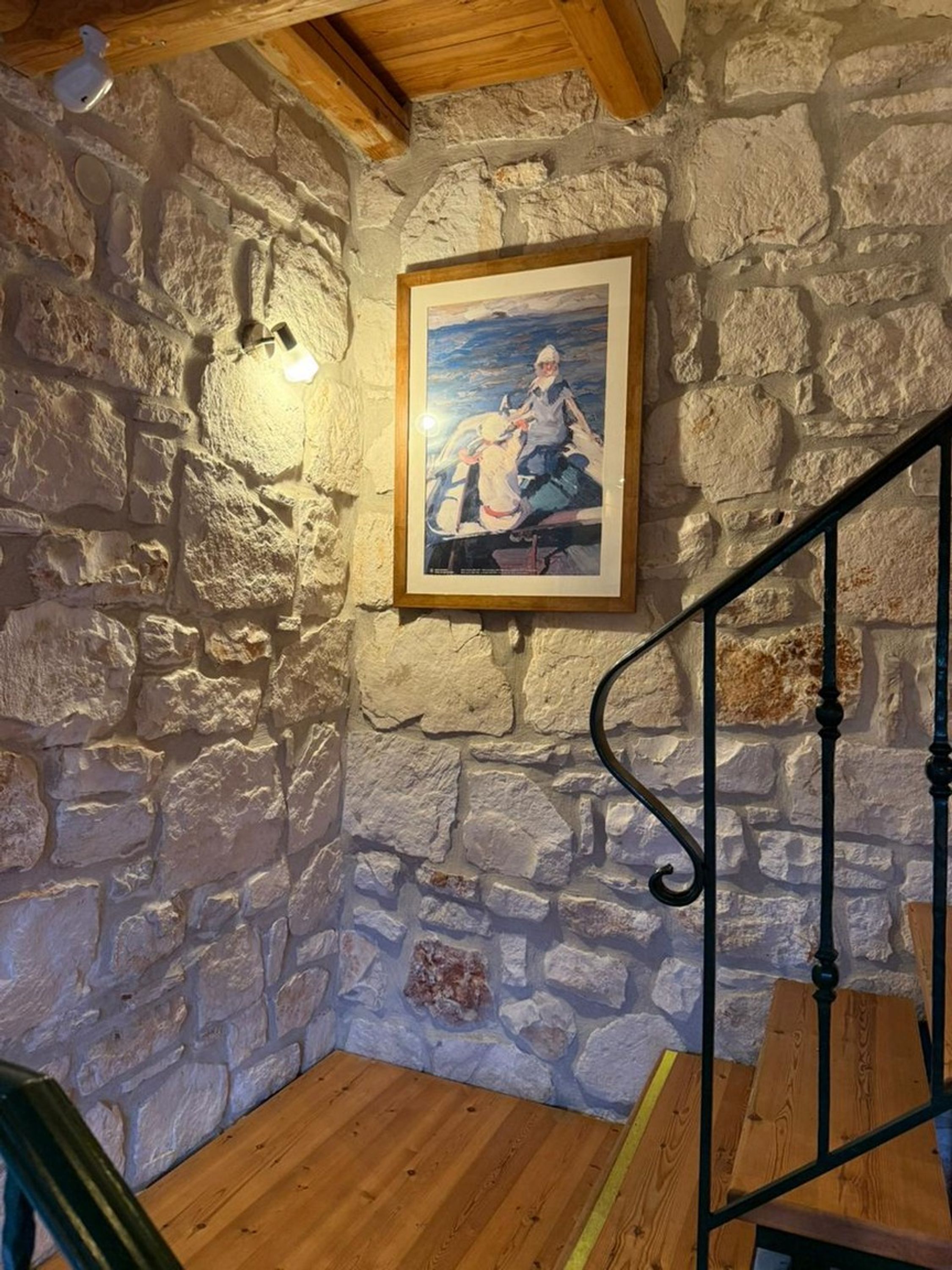 Una stanza rustica con parete in pietra, pavimento in legno e una scala con ringhiera in metallo.