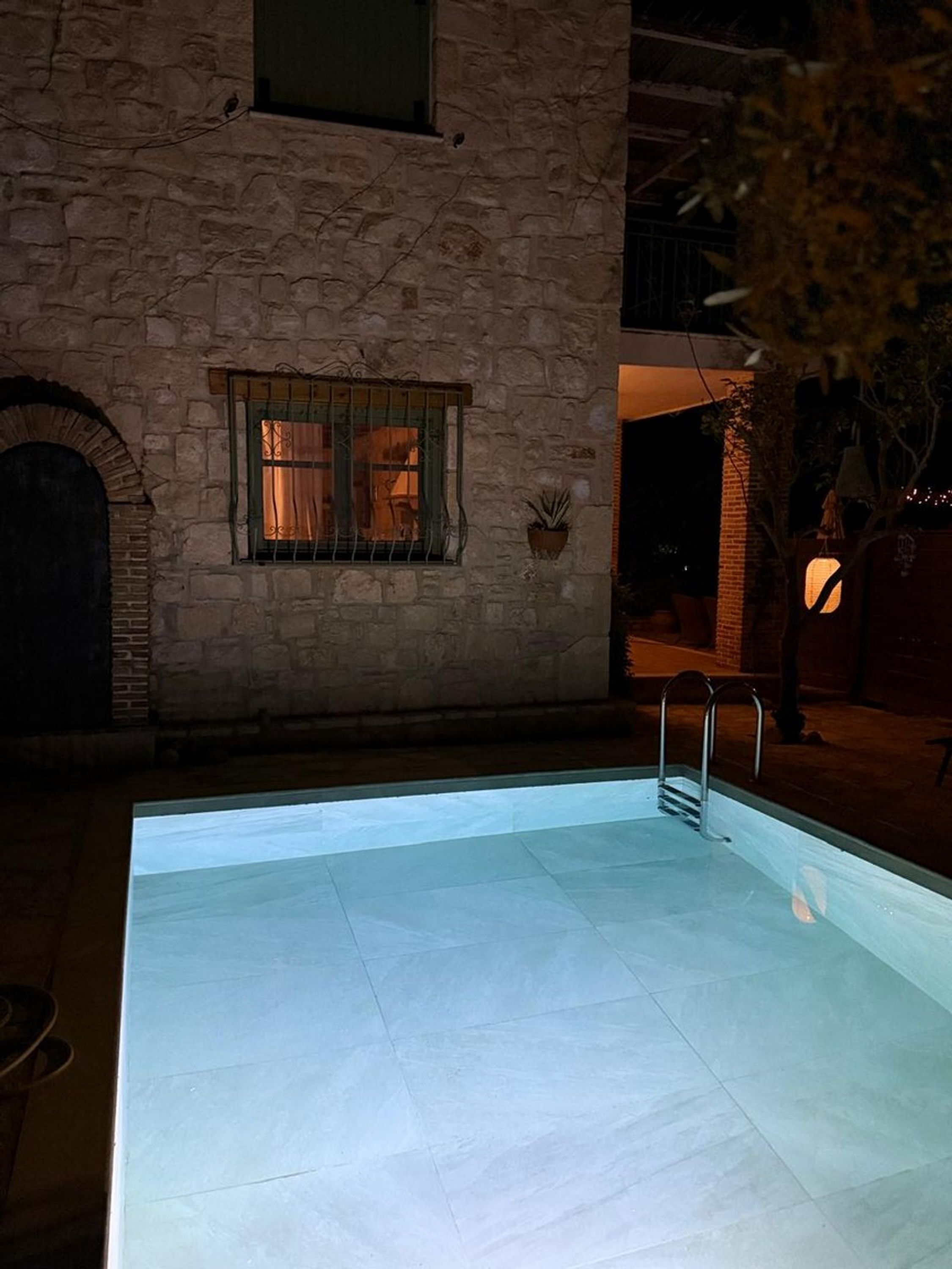 Un bâtiment en pierre avec une piscine, une fenêtre avec des rideaux et une petite plante en pot.
