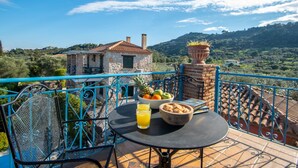 A terrace with a table set for breakfast, a view of a stone house, and a lush landscape in the background. - Valory s Stone Tower (Zakynthos)